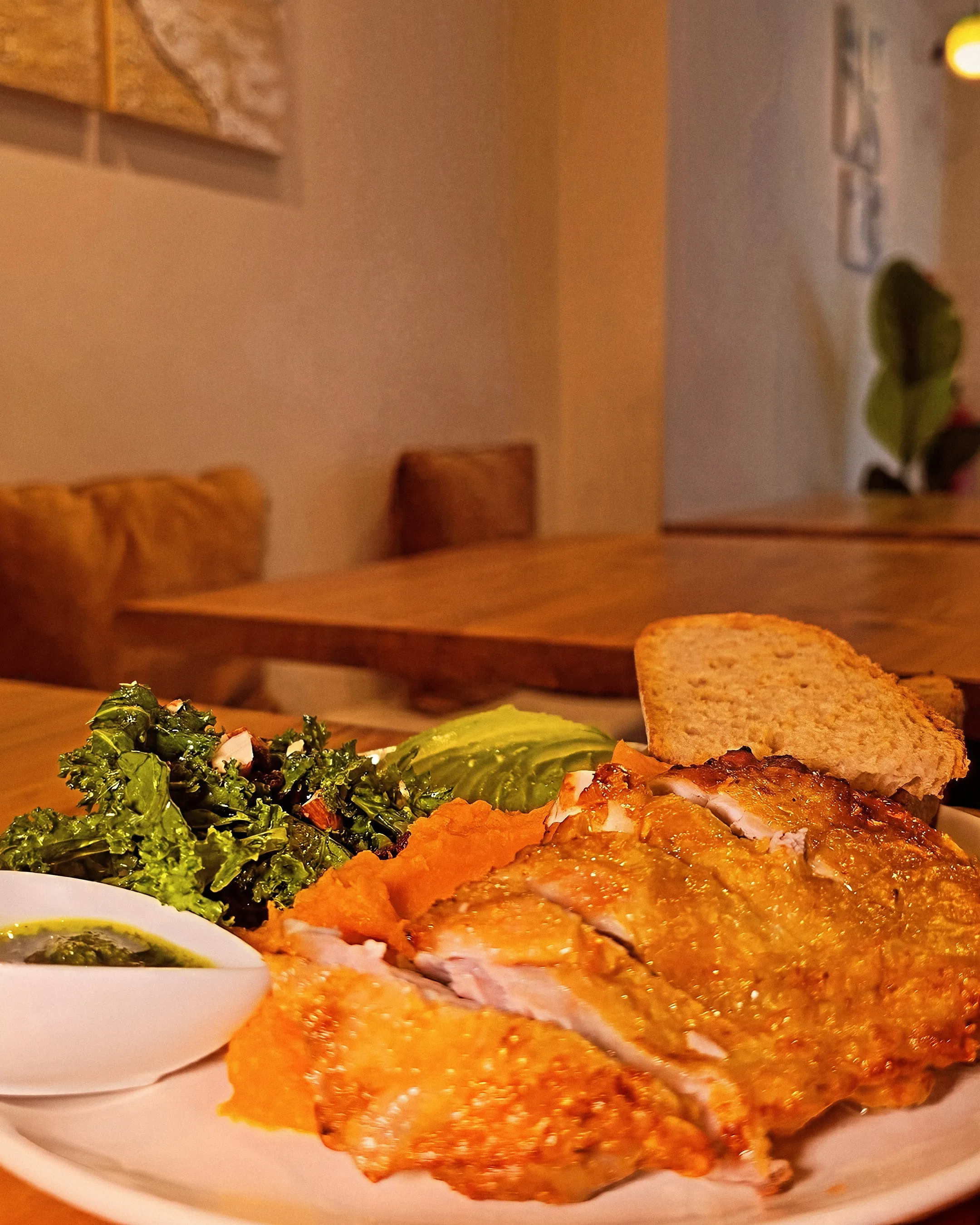 The Golden Chicken con kale, aguacate, puré de boniato y tostada; detrás, las mesas de madera y los cojines del local